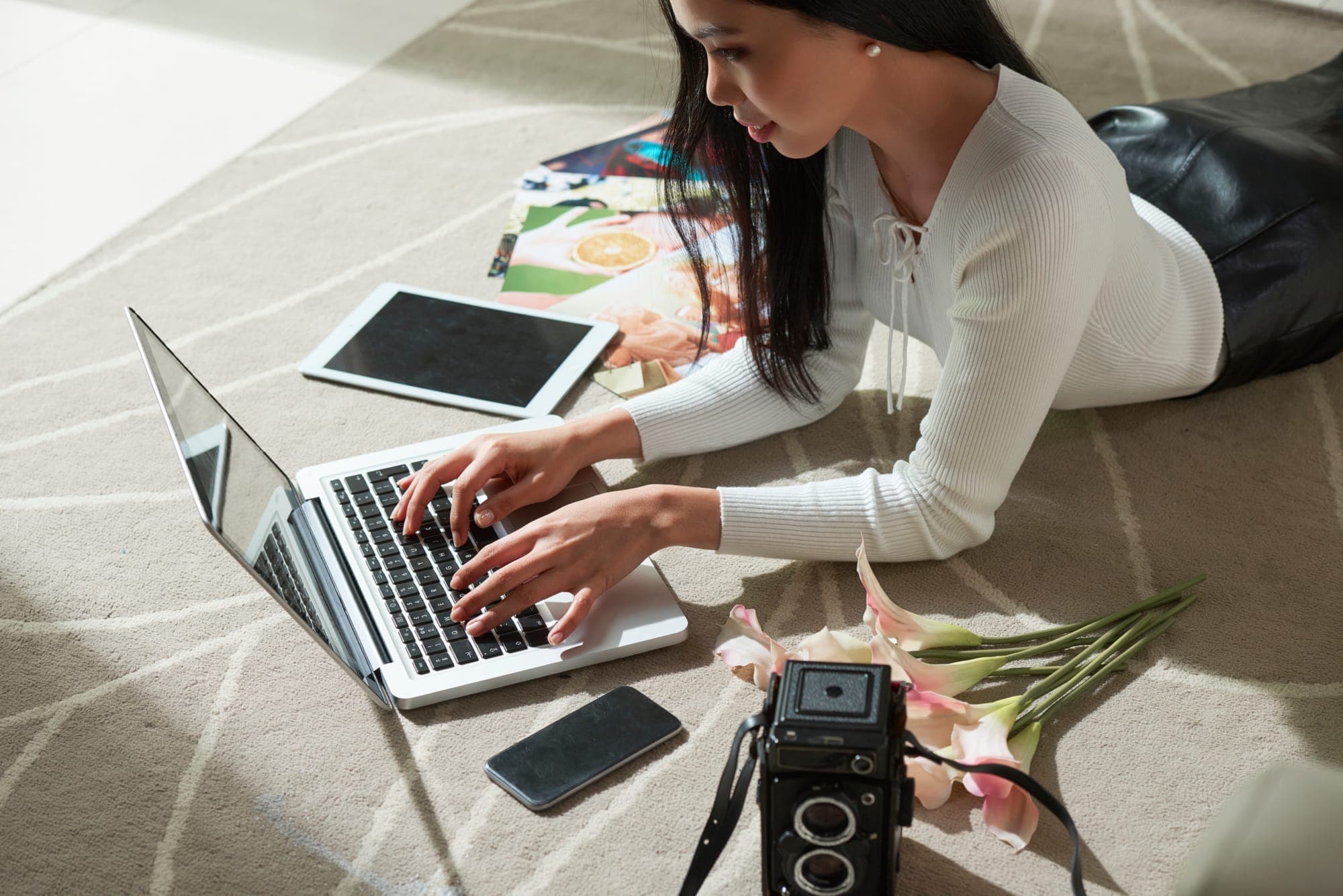 Young woman working on laptop while laying on the floor.